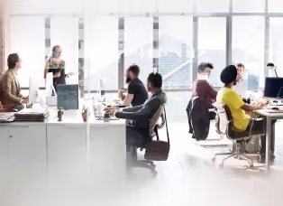 A team at desks in an open-plan office with city views through the windows