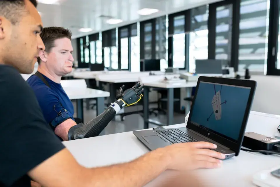 Two people using laptop, one is disabled and is using a engineered arm to function